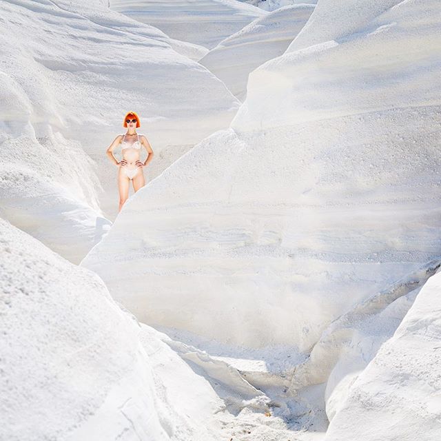 A woman in a bikini and sunglasses poses in a white, canyon-like landscape for a fashion editorial.