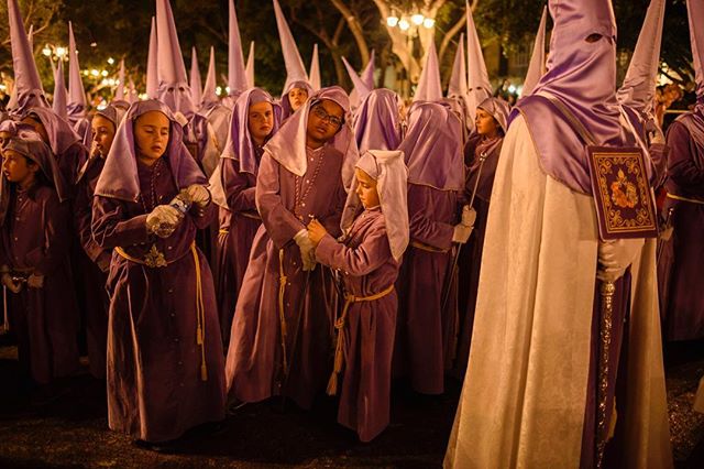 A group of people in purple robes and hoods participates in a nighttime procession.