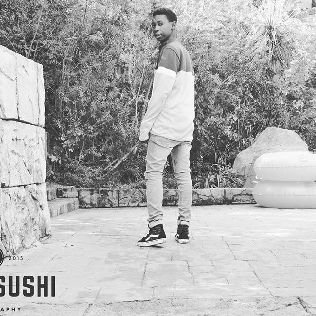 A young man in a casual outfit stands in a backyard in black and white.