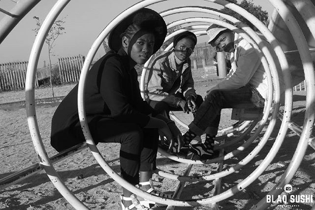 Three people are sitting in a playground structure on a sunny day in a black and white shot.