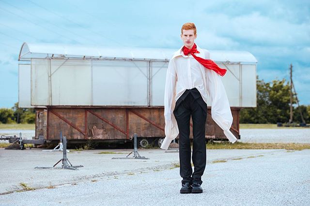 A redhead poses in an editorial fashion shoot with a white shirt and red scarf outdoors.