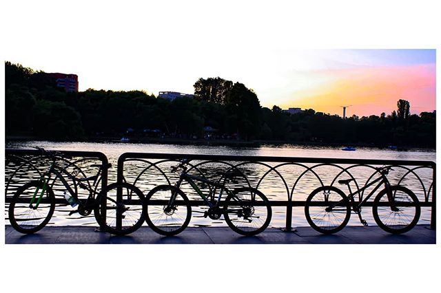 Silhouetted bicycles stand at a rack by a lake at sunset, creating a calm and scenic view.