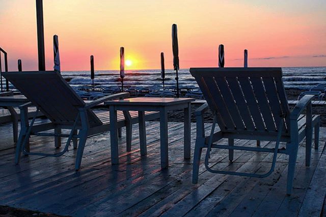 A peaceful sunset over the ocean, with deck chairs and tables on a wooden deck.