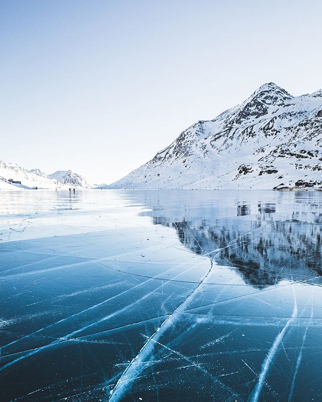 A frozen lake reflects the snowy mountains, creating a tranquil winter landscape.