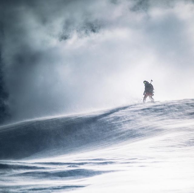 A lone climber ascends a snowy mountain in a winter storm, highlighting endurance and the spirit of adventure.