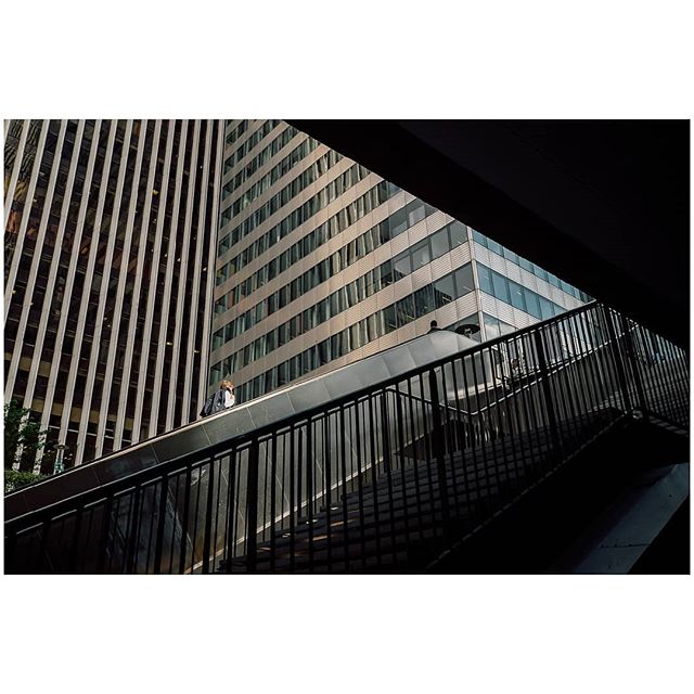 A low-angle view of a person on an escalator between tall buildings in an urban setting.