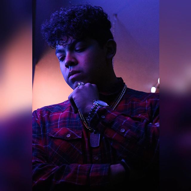 Portrait of a young man in a plaid shirt with jewelry under moody, colorful lighting.