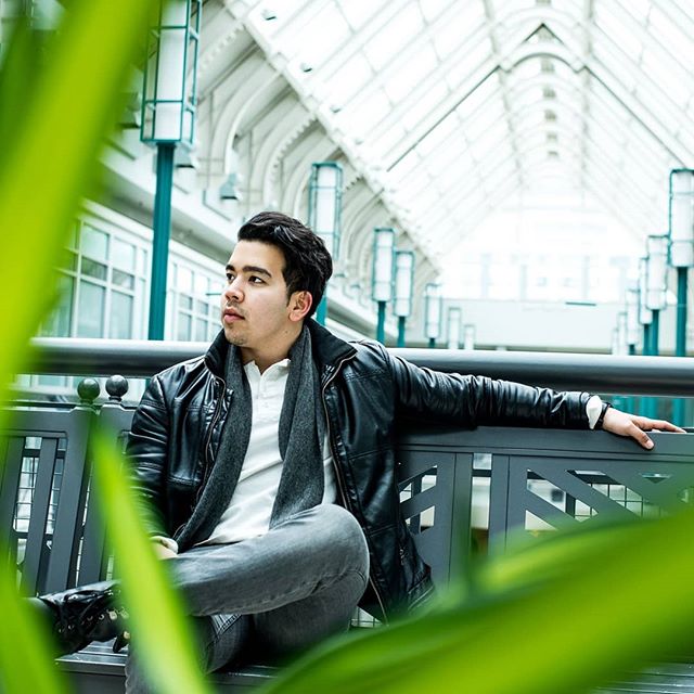 A man in a black jacket sits on a bench in a modern building.