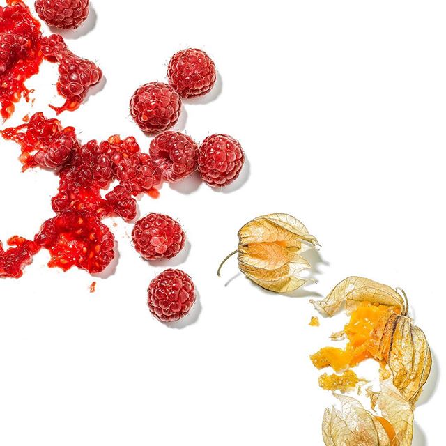 Fresh raspberries and golden berries sit on a white surface, perfect for healthy food ads and website content.