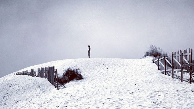 A person standing on a sand dune against a cloudy sky, a minimalist black and white photograph.