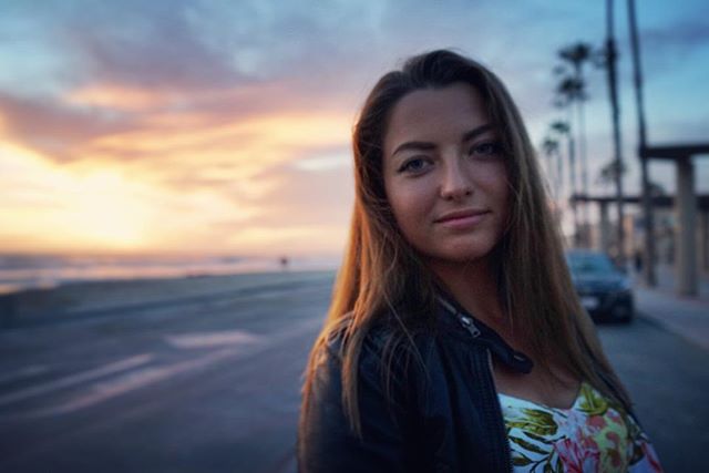 A woman poses at the beach during a colorful sunset. The focus is on her face.