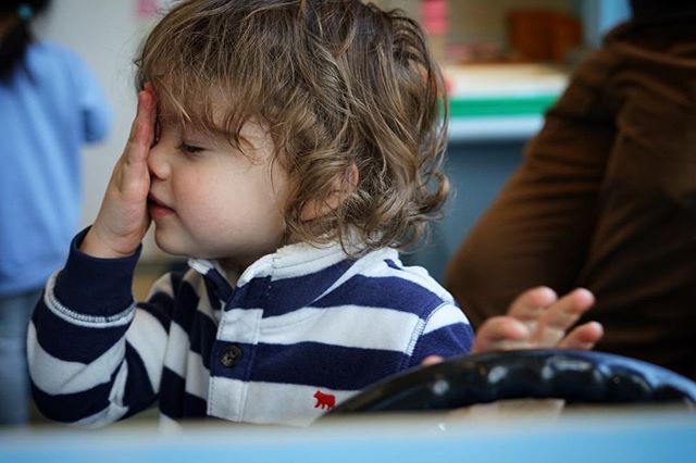 A toddler with curly hair rests their face on their hand, looking peaceful in soft light.