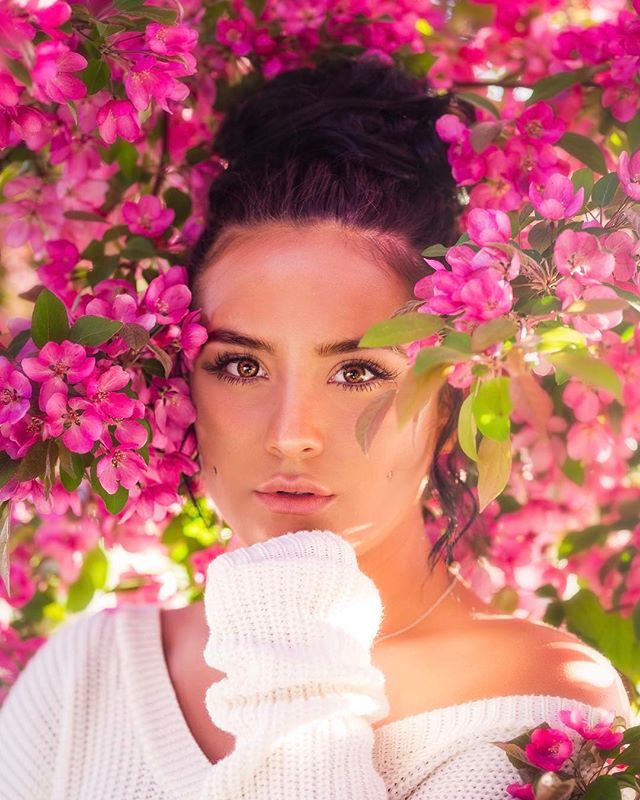 A serene woman poses with pink blossoms, ideal for beauty and wellness campaigns.