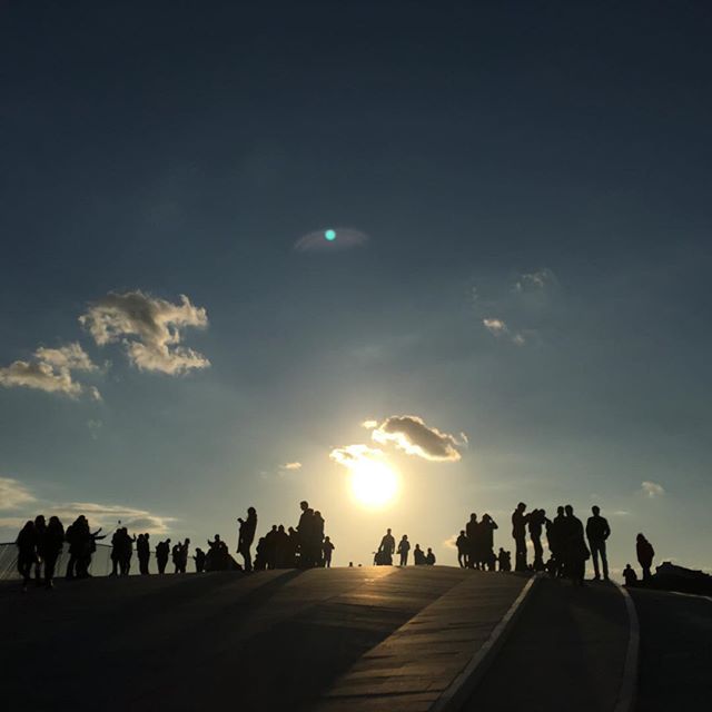 Silhouettes of people gather to watch a vibrant sunset over a cityscape, creating a serene and harmonious scene.