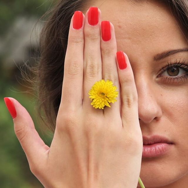 Close-up of a woman with a yellow flower on her finger and red fingernails.