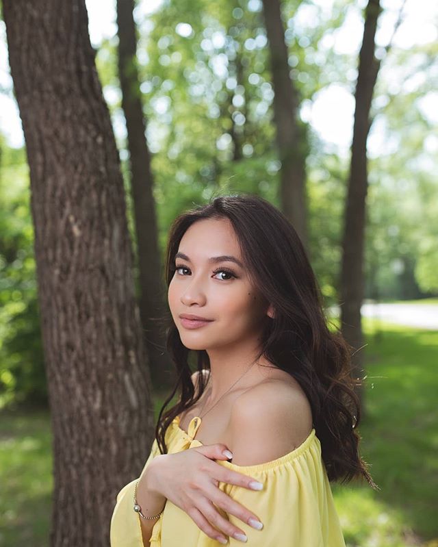 A young woman in a yellow top poses in a sun-dappled forest for a serene outdoor portrait.