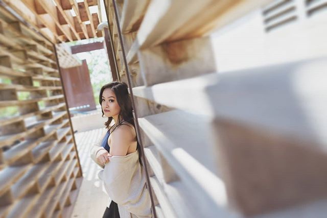A woman poses inside of a wooden structure with geometric designs for an image highlighting the modern design, travel, and lifestyle.