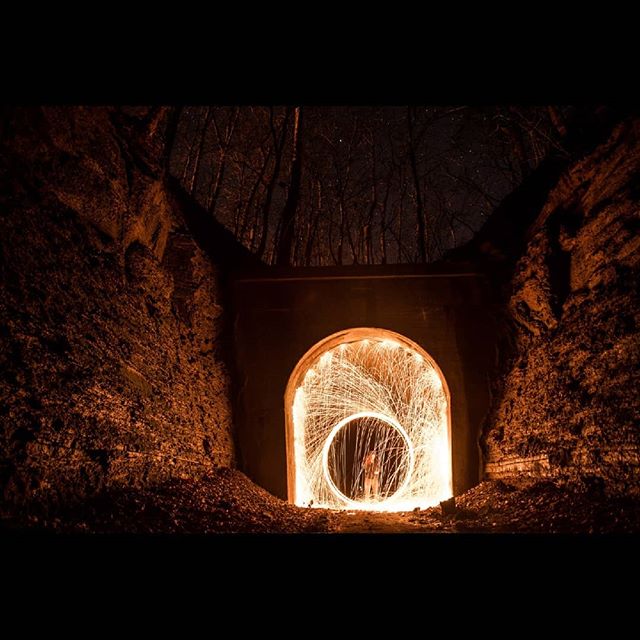 A person stands inside a tunnel with light painting, creating a unique and mysterious scene in the dark.