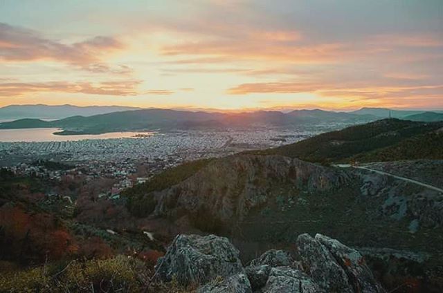 Panoramic view of a city and mountains under a colorful sunset, showcasing a tranquil and scenic landscape.