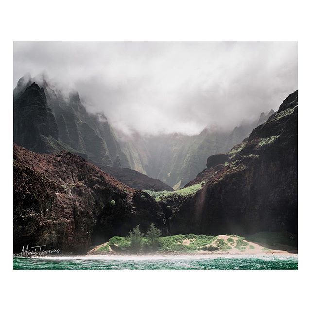 A stunning coastal landscape featuring dramatic mountains shrouded in mist, lush vegetation, and a tranquil ocean.