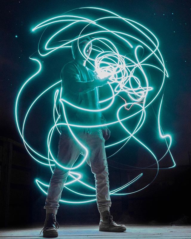 A person light painting at night with swirling blue neon lights.
