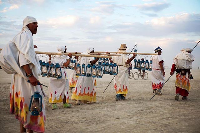 People in robes carry lanterns across a desert during a festival, showcasing a unique cultural event.
