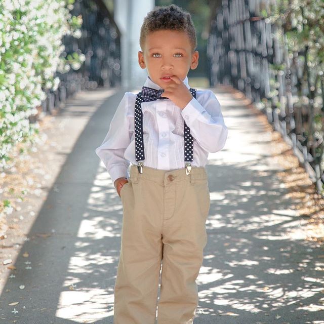 A young boy poses in a formal outfit on a tree-lined path, showcasing children's fashion.