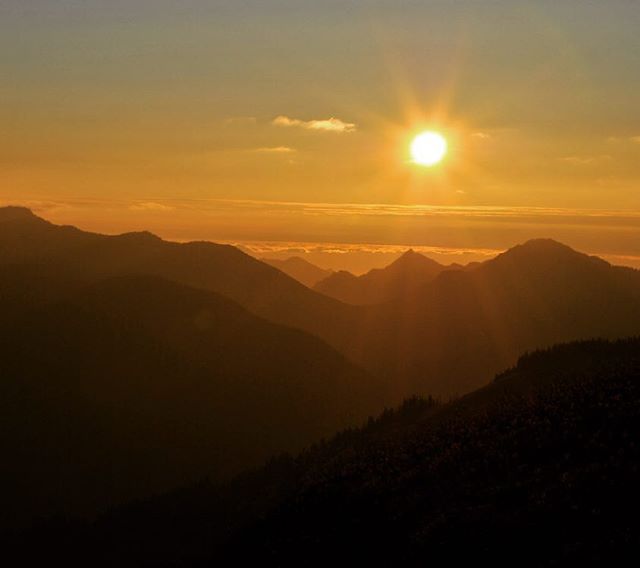 Golden sun shines over silhouetted mountain peaks in a serene landscape.