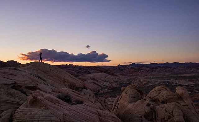 A lone person stands atop rocky terrain, silhouetted against the sunset in Valley of Fire State Park.