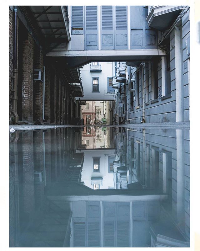 An urban alleyway with reflections of buildings in a puddle creates a serene and atmospheric city view.