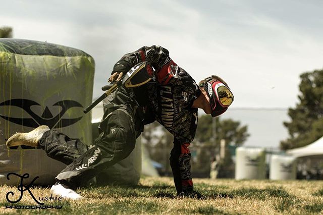 A paintball player in action on a grass field, wearing protective gear and holding a paintball gun.