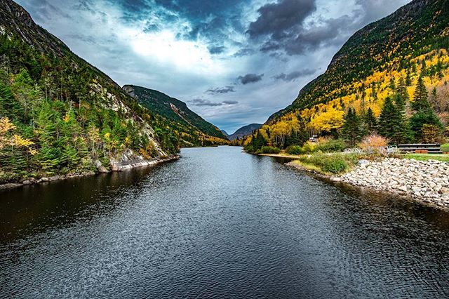 Scenic view of a calm lake surrounded by mountains and trees under a cloudy sky.