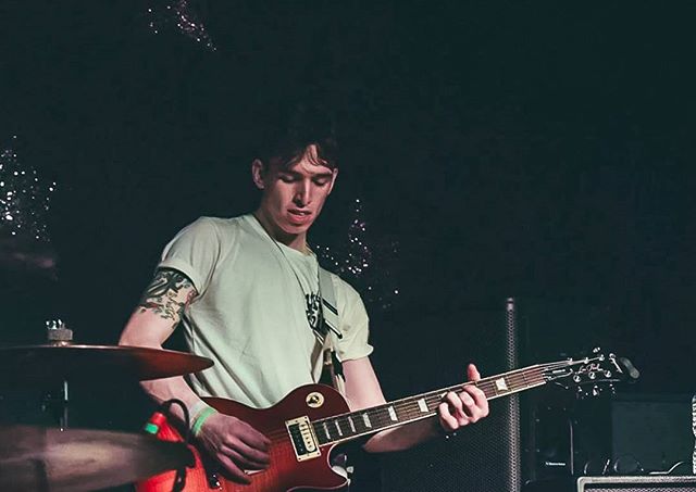 A guitarist performs on stage in a dimly lit music venue.