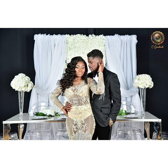 A stylish couple poses in formal attire at an elegant event, exuding love and sophistication in a modern indoor setting.