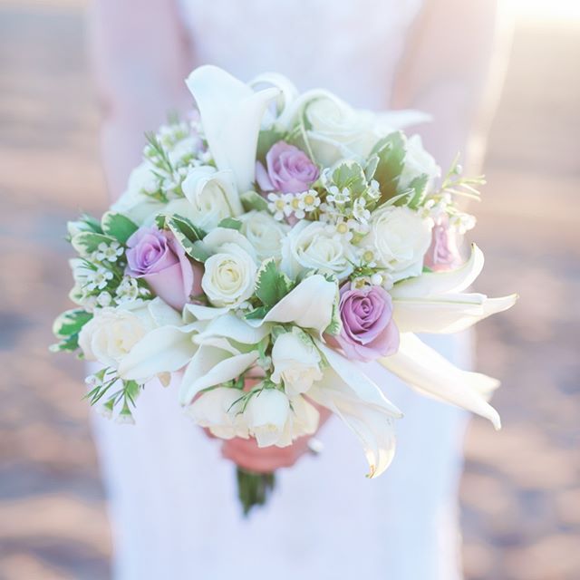 A beautiful bridal bouquet with white lilies and roses, with touches of purple roses, perfect for a beach wedding.