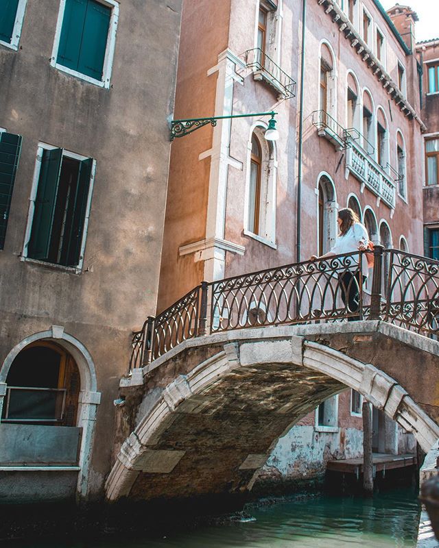 A woman walks across a bridge in Venice, Italy, with old buildings lining the canal.