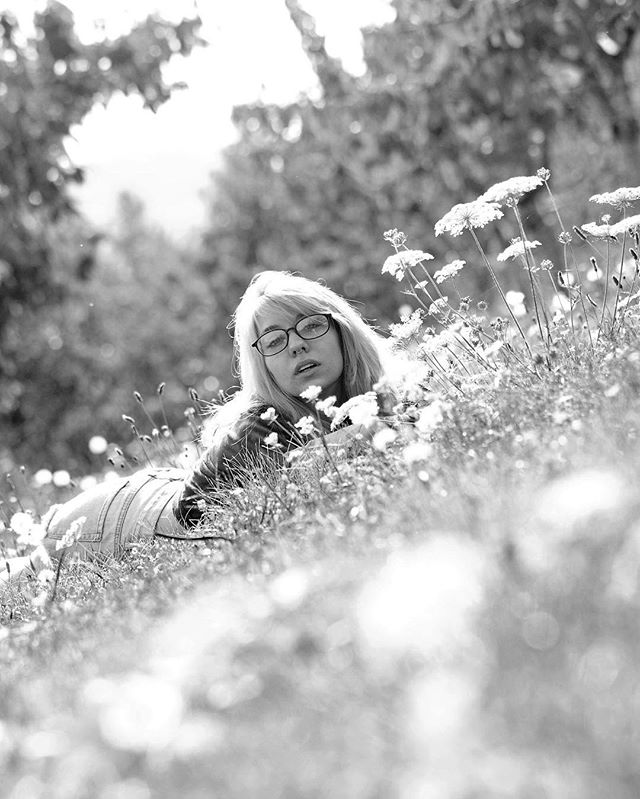 A woman with glasses relaxes in a meadow filled with white flowers, captured in black and white.