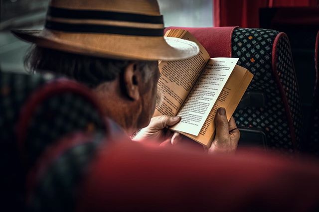 A man wearing a hat is engrossed in reading a book, creating a moment of quiet contemplation.
