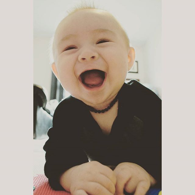 A happy baby laughs while lying on their stomach indoors.