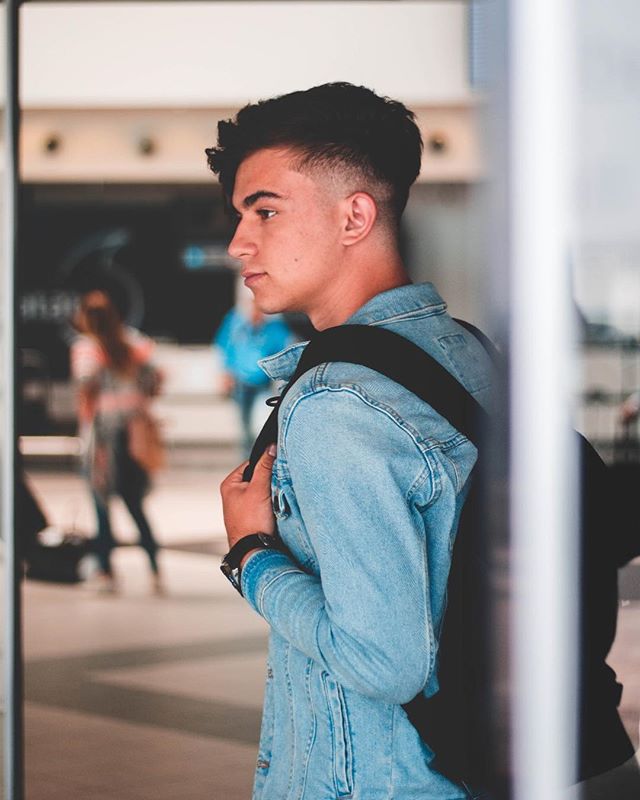 Young man in denim jacket with a backpack looking out in an urban setting.