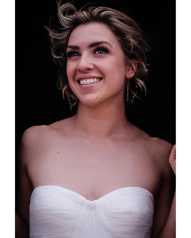 A smiling woman in a white strapless dress looks up in a bright, natural light studio portrait.