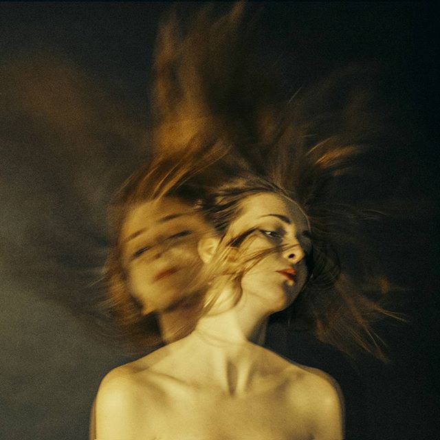 An artistic portrait of a woman with blurred motion evokes mystery and emotion against a dark background.