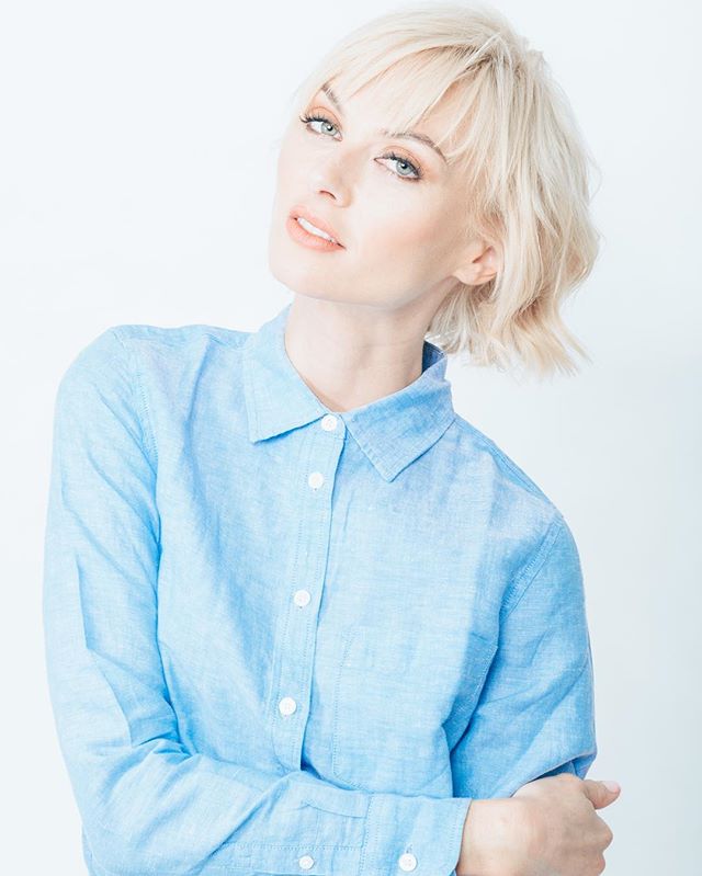 A blonde woman in a blue shirt poses against a white background for a professional portrait.