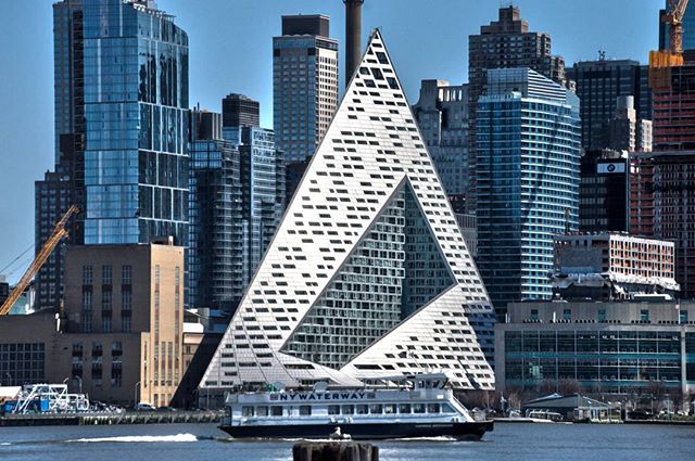 Modern VIA 57 West building in Manhattan, with a boat sailing in front of the waterfront cityscape.