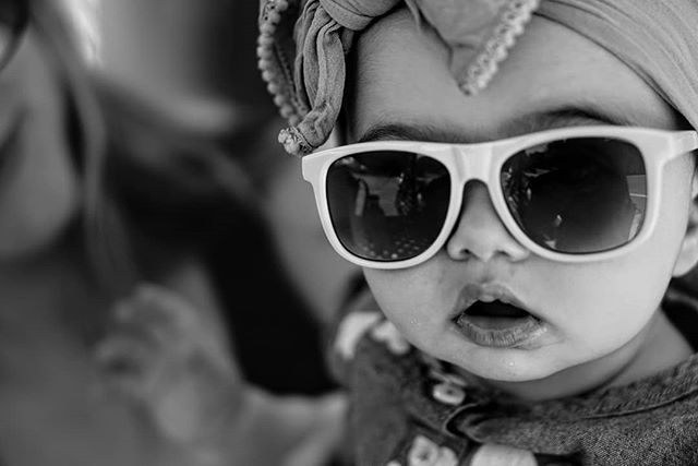 A stylish baby wearing sunglasses and a headband strikes a pose in this monochrome close-up.