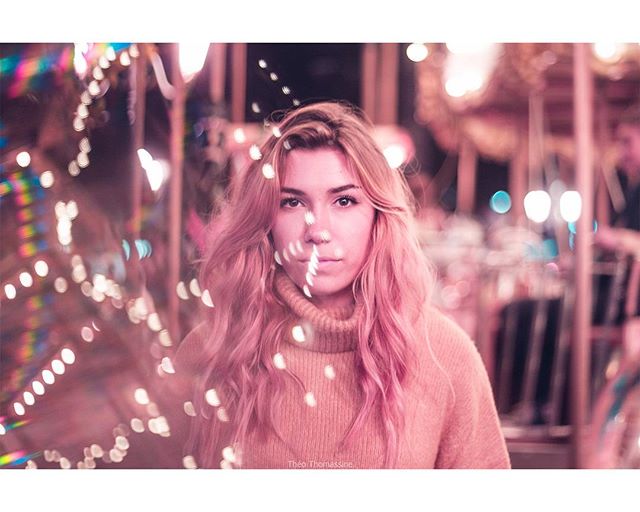 A woman with pink hair poses in front of a carousel, creating a dreamy, intimate atmosphere.