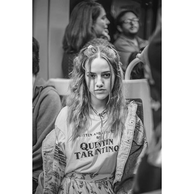 A young woman with a serious expression sits on public transport in a black and white image.