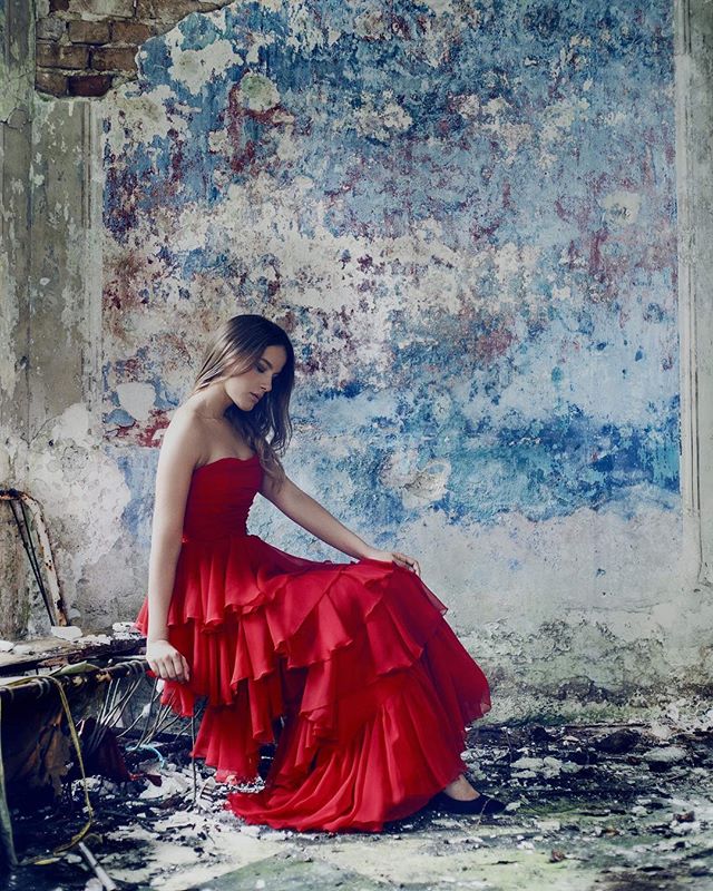 A woman in a red dress sits in an abandoned building, creating a dreamy and emotive scene.