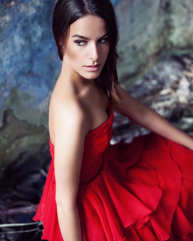 A woman in a red dress poses in a studio setting, creating an elegant, dreamy atmosphere.