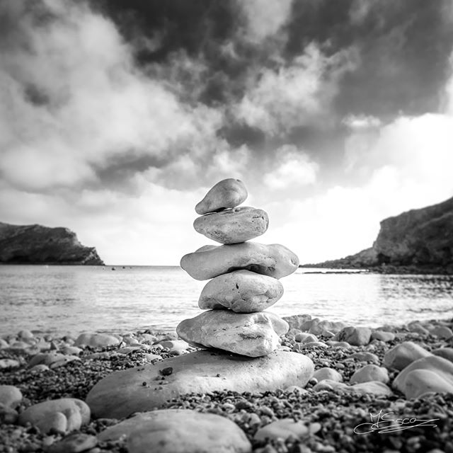 A stack of balanced stones on a pebble beach creates a calming, zen scene against a cloudy sky.